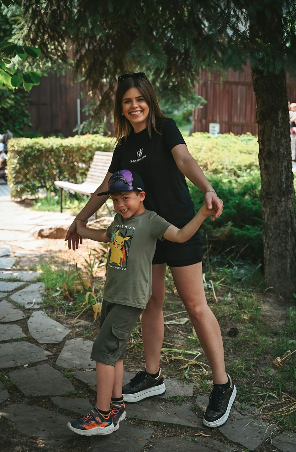 A woman and young boy stand smiling on a stone path.